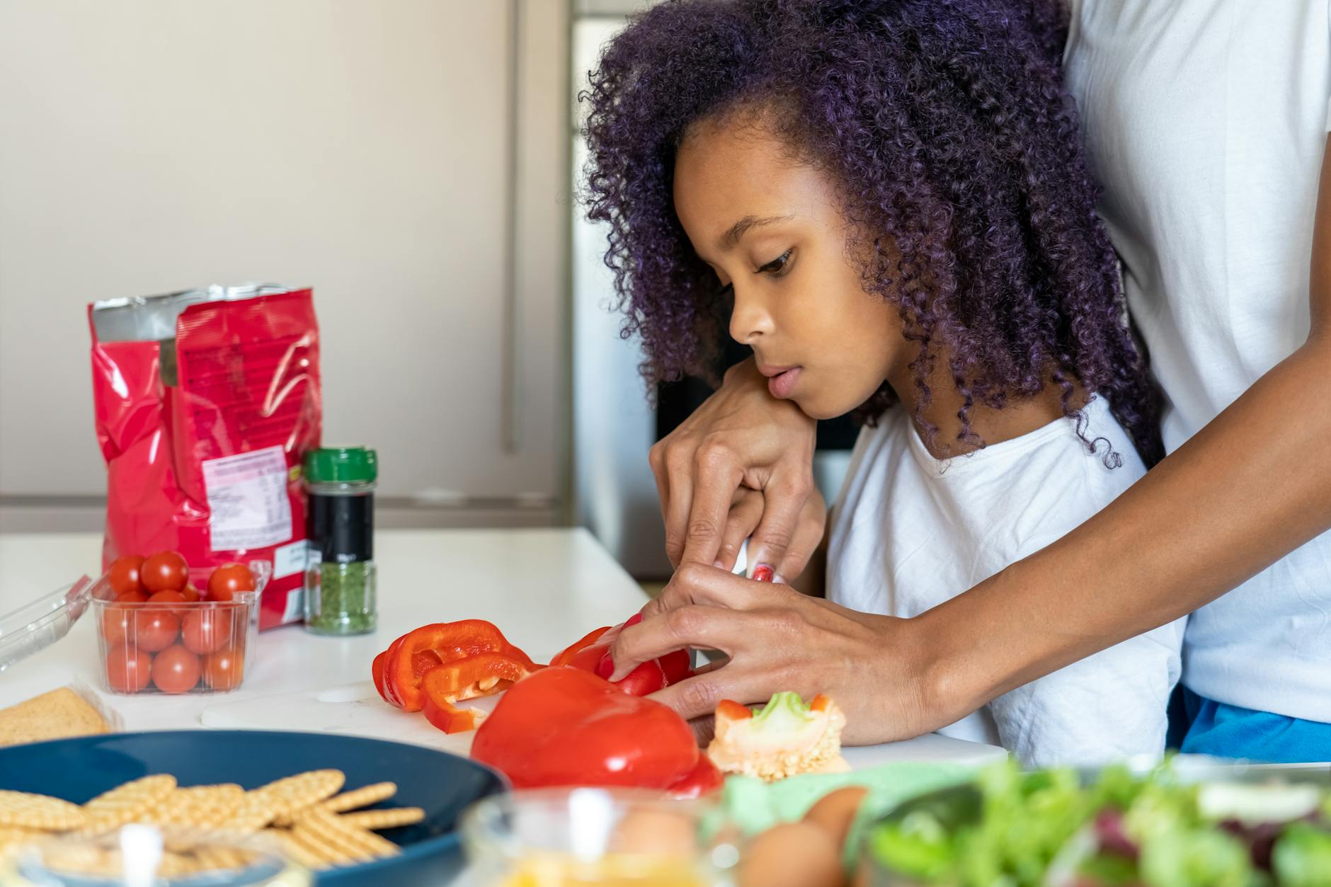 a parent helping a girl slice a bell pepper