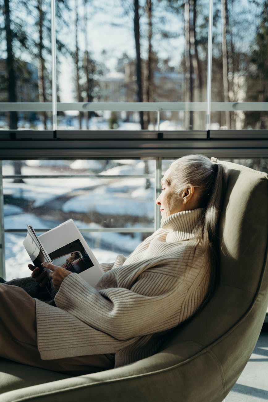 a woman reading a book while sitting beside the window